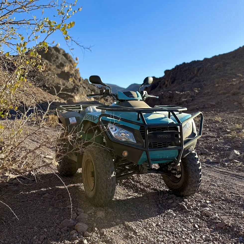 A turquoise quad parked on a rocky trail between desert hills